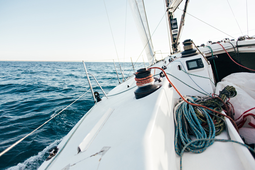 Deck of professional sailboat or racing yacht during competition on sunny and windy summer day, moving fast through waves and water, with spinnaker up, and ropes tied around winch